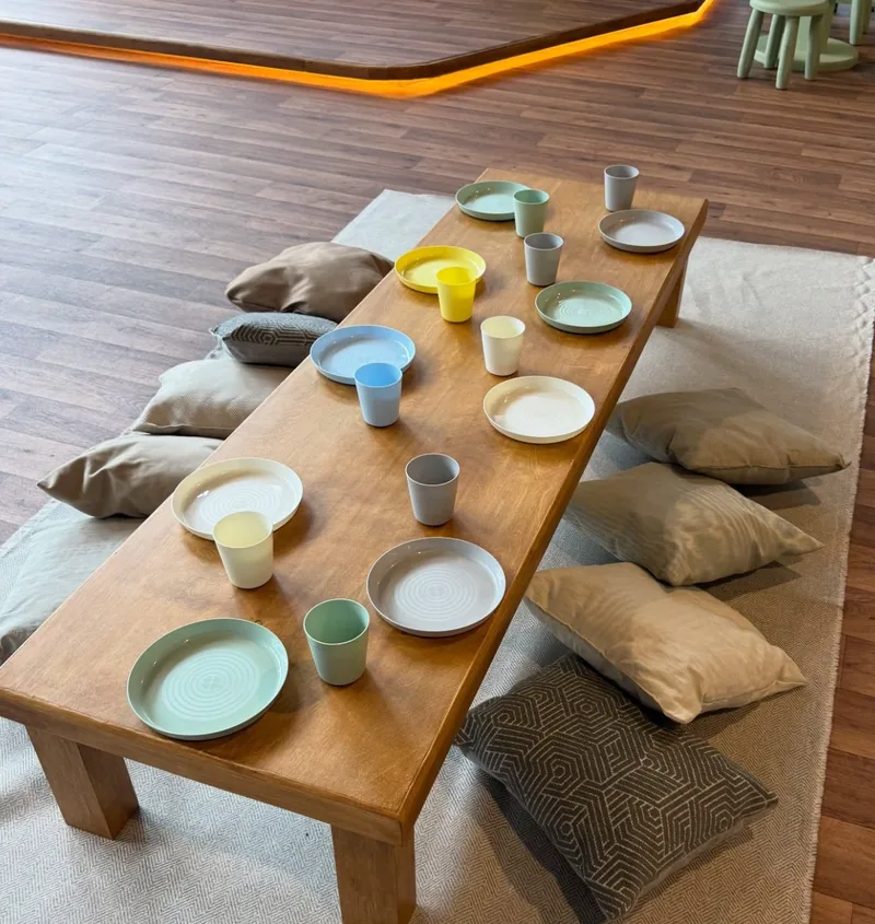 Mesa baja de madera con platos y vasos de colores lista para los niños
