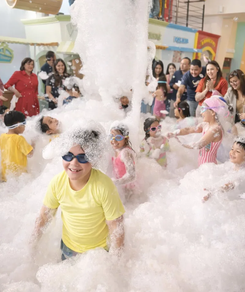 Niños con goggles jugando en la Fiesta de Espuma mientras sus papás los ven y aplauden